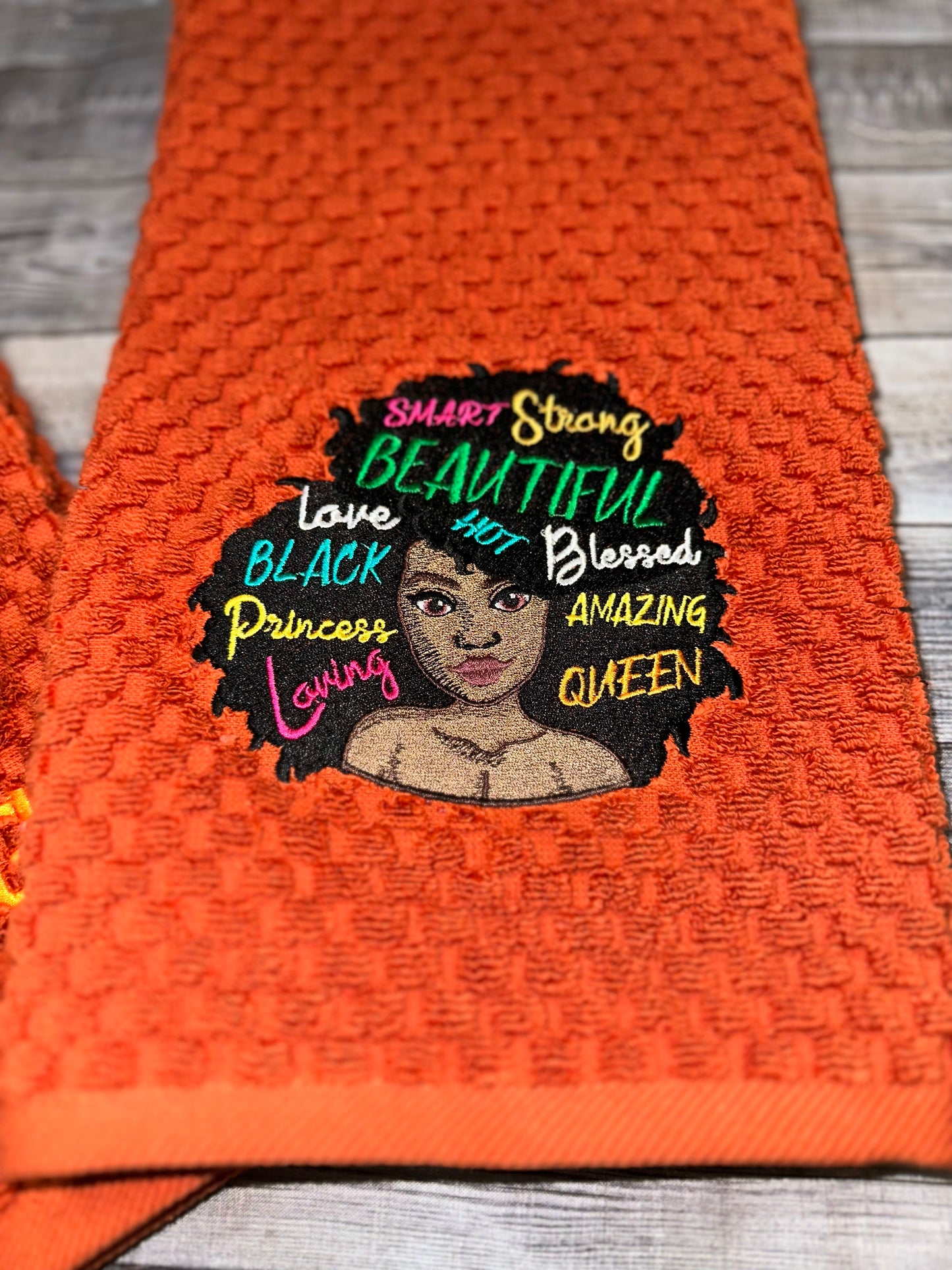 Black woman with empowered words in hair on embossed rust orange towels. embroidered