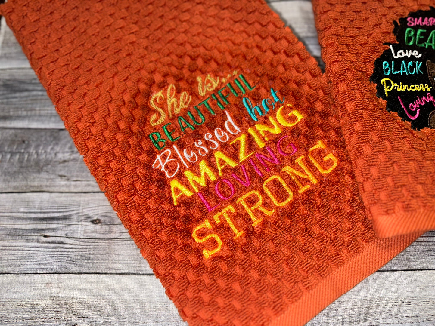 Black woman with empowered words in hair on embossed rust orange towels. embroidered