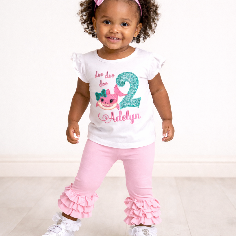Child wearing a white shirt with a shark design and pink pants on a white background