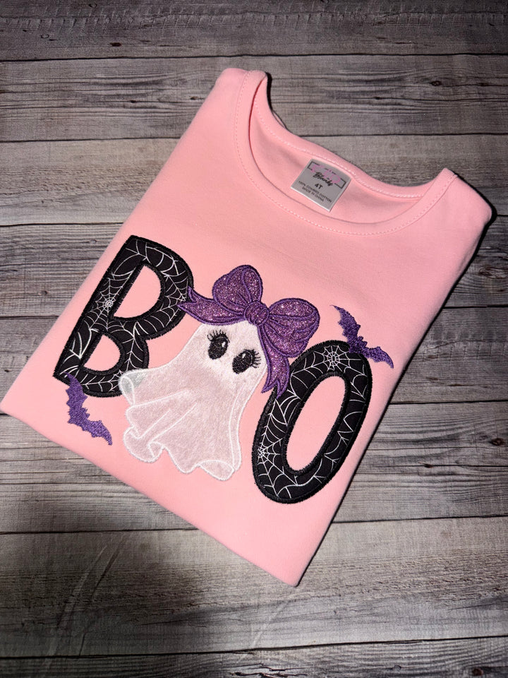 Pink girls Halloween shirt featuring an embroidered ghost with a glitter purple bow, spiderweb Boo appliqué letters, and embroidered bats.