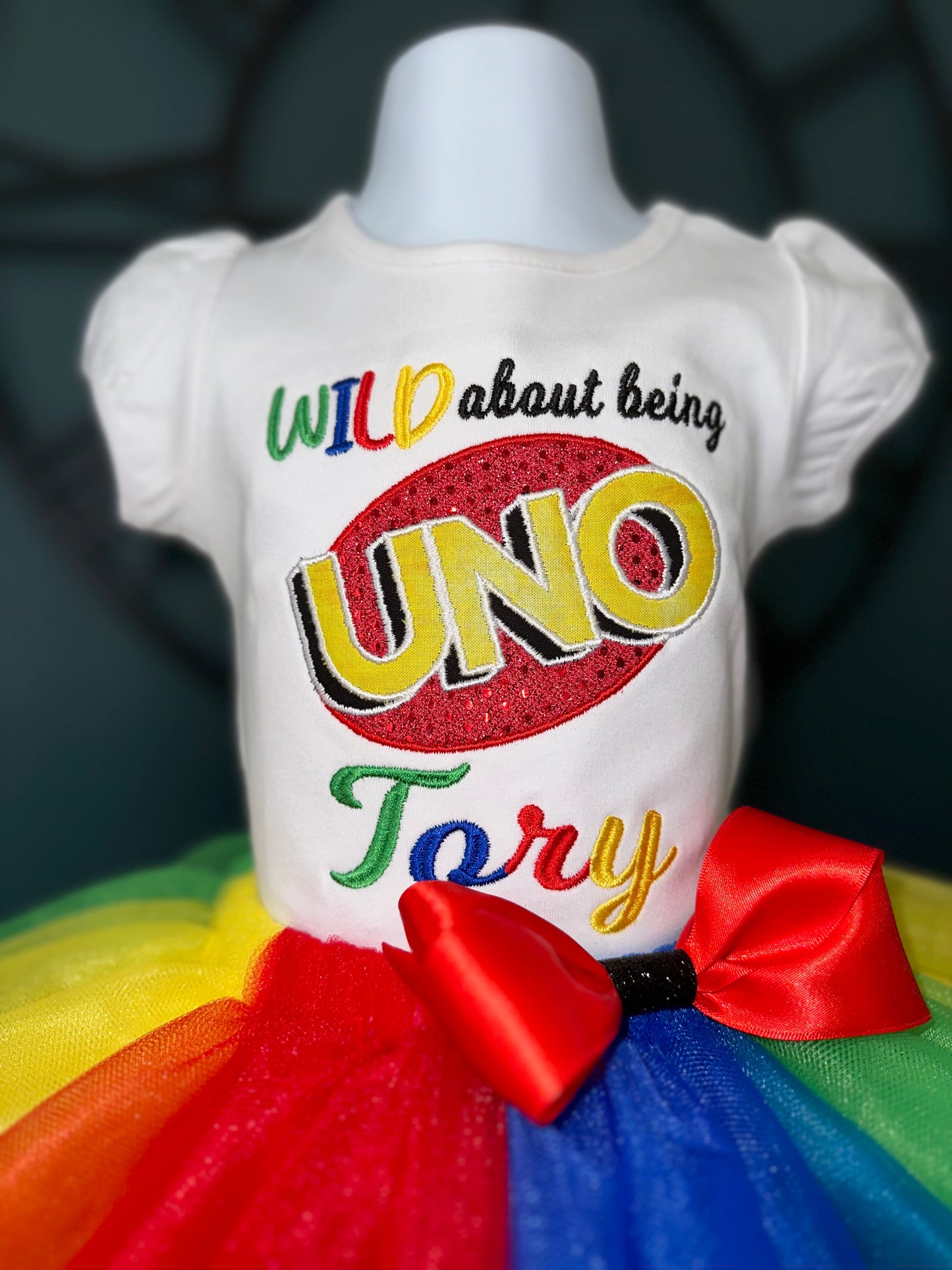 personalized wild about being uno theme outfit, ribbon trimmed red, blue, green, and yellow tulle skirt with red waist bow. embroidered white shirt with uno theme logo
