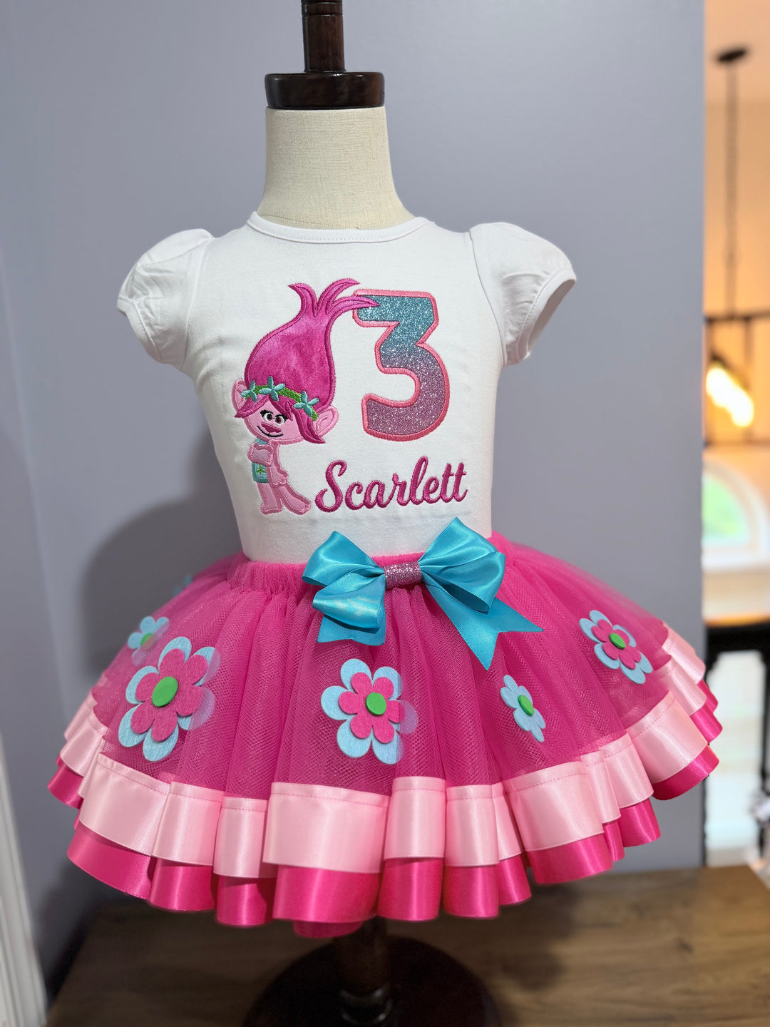 Pink girls Trolls birthday outfit featuring Poppy shirt, floral tutu skirt, and blue satin bow