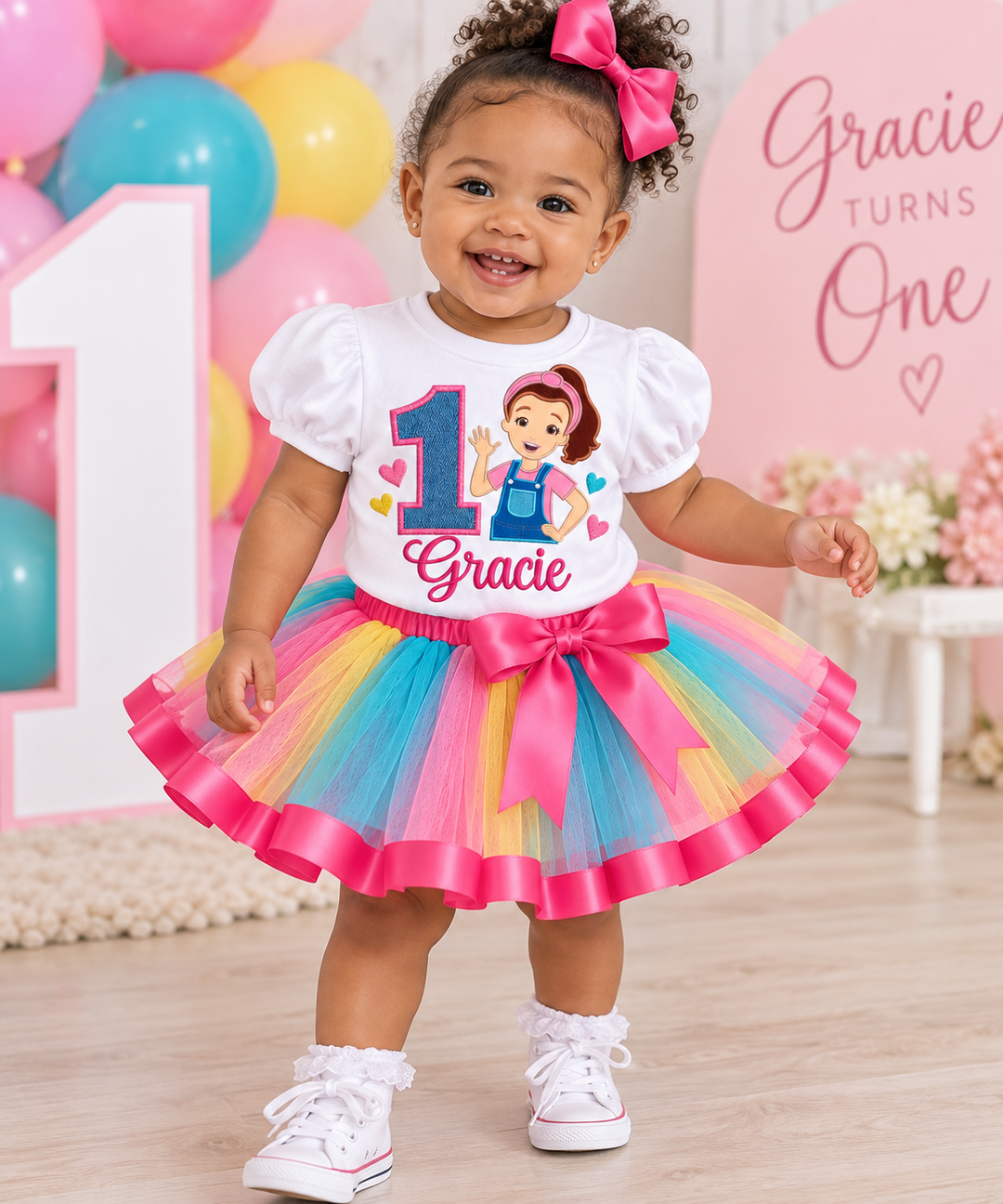 Personalized Ms. Rachel first birthday outfit for girls featuring a puff sleeve shirt with denim number one and a colorful tutu with pink ribbon trim and waist bow