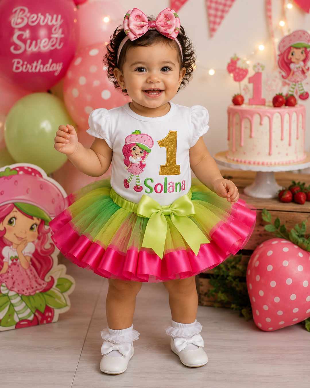 Child in a colorful birthday outfit with a Strawberry Shortcake theme, standing in front of a birthday cake and balloons.
