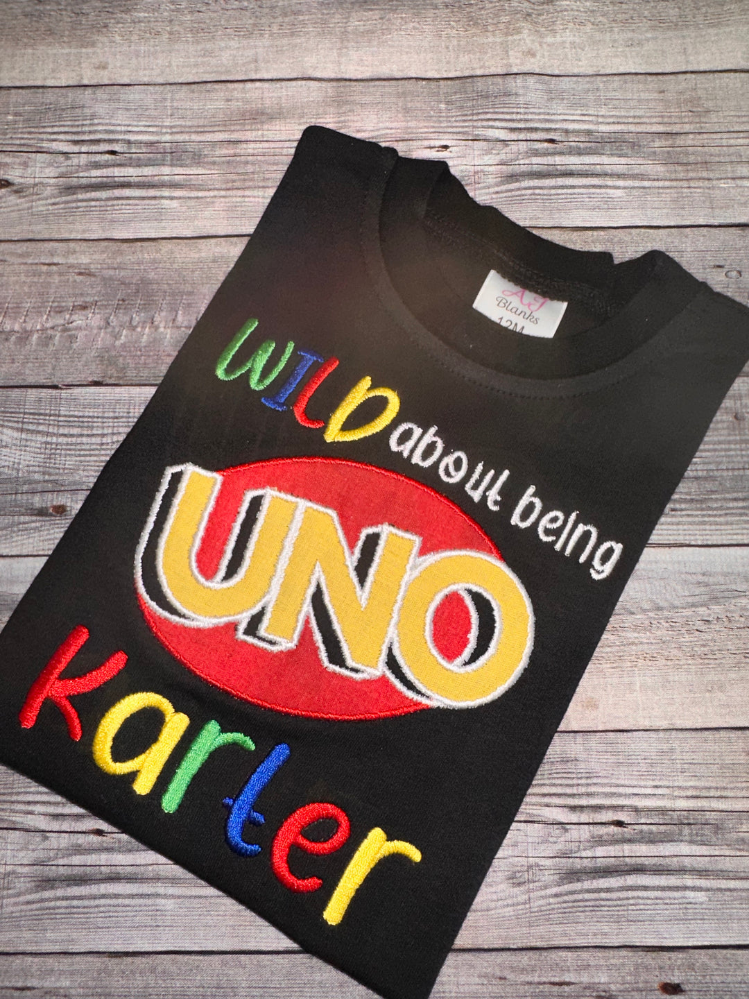 Custom Wild About Being UNO birthday shirt on black fabric featuring colorful embroidery and personalized name for a first birthday celebration.”