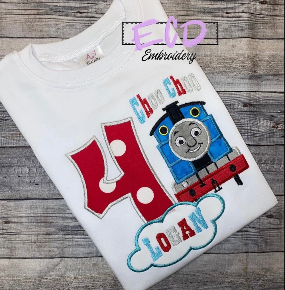 A personalized white birthday shirt with a toy train design and the name 'EIAN' embroidered on it.