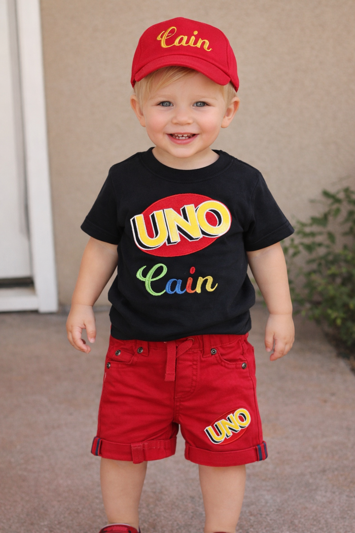 Personalized UNO birthday shirt set for boys with colorful embroidered UNO lettering, red shorts, and matching embroidered birthday cap.