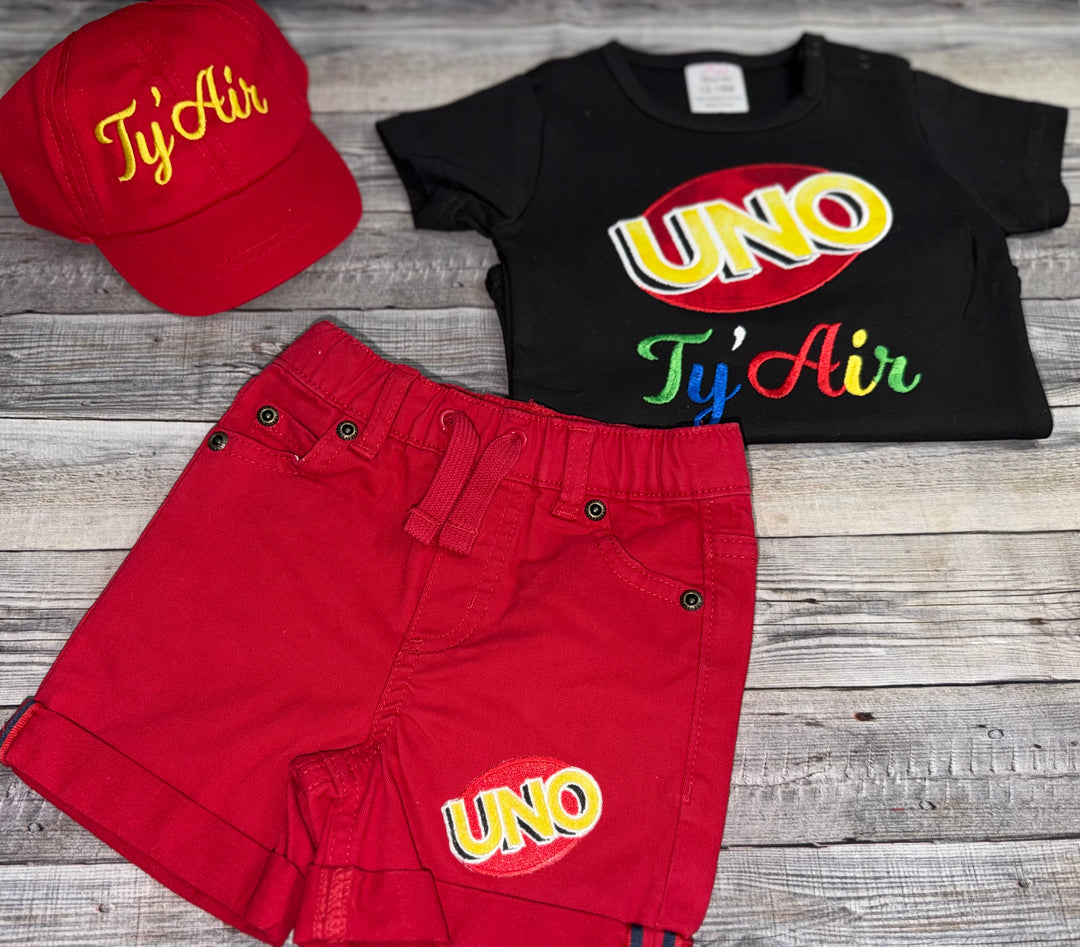 Custom UNO One birthday outfit for a toddler boy featuring colorful UNO embroidery, personalized name shirt, red shorts, and matching hat.