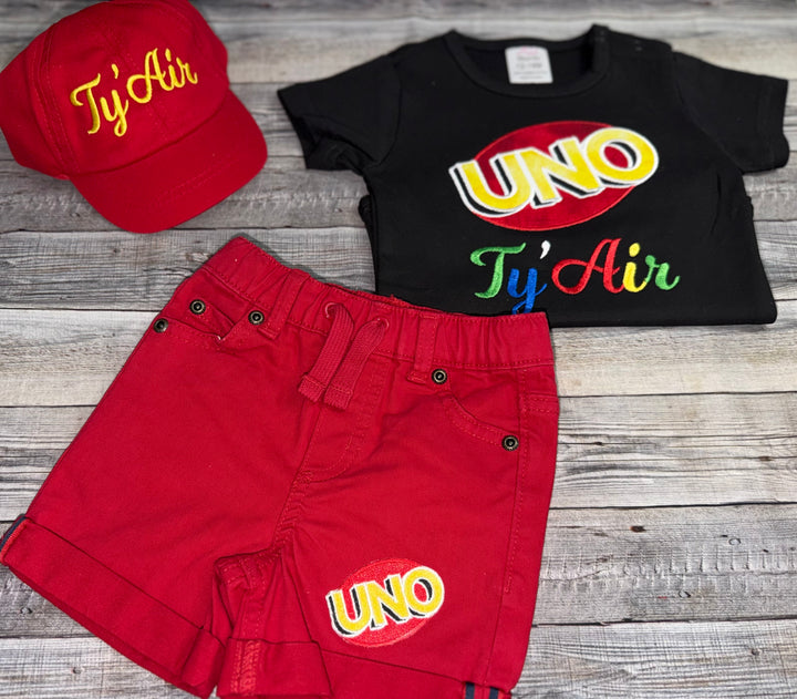 Custom UNO One birthday outfit for a toddler boy featuring colorful UNO embroidery, personalized name shirt, red shorts, and matching hat.