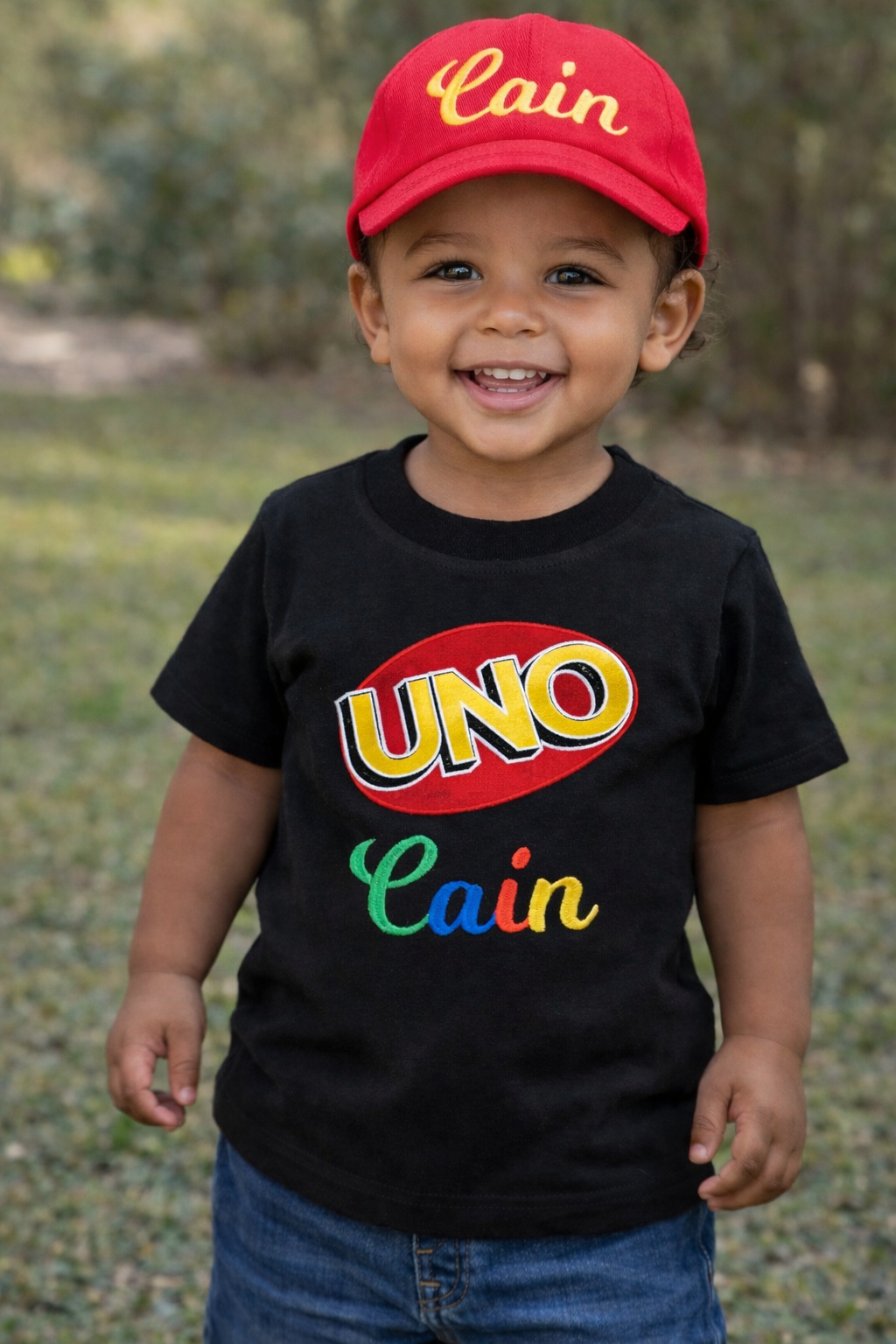 Toddler boy UNO birthday outfit featuring a personalized embroidered black shirt, red shorts, and red UNO hat for a fun birthday celebration.
