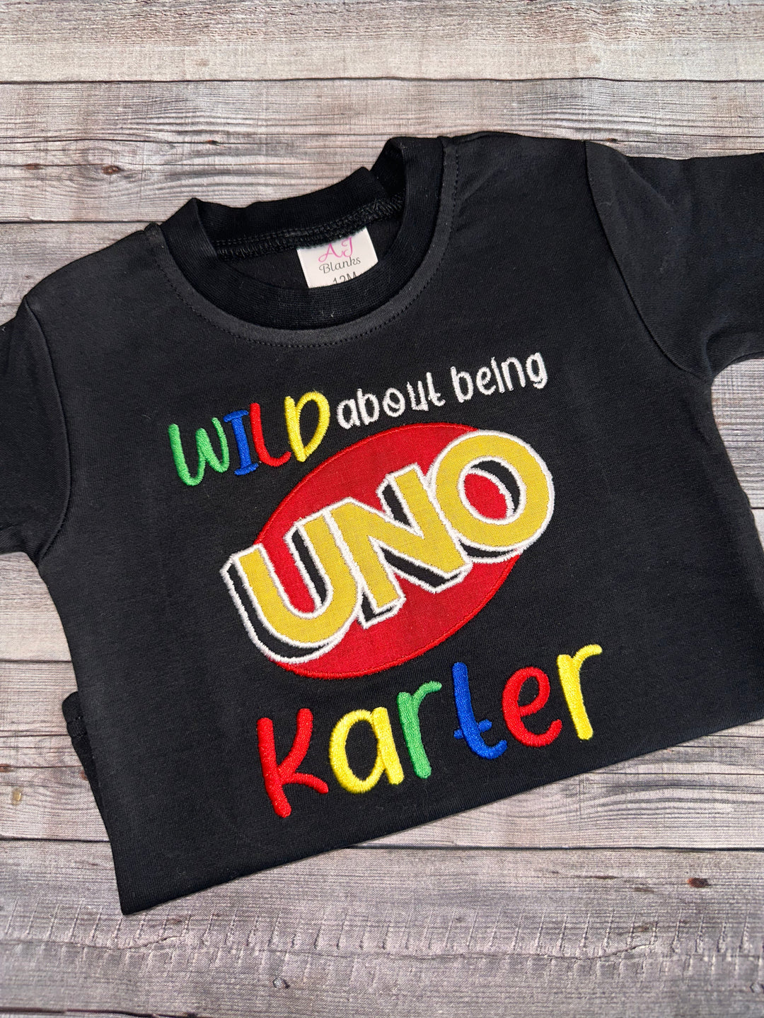 Personalized black UNO first birthday shirt with custom embroidered name and colorful Wild About Being UNO design for boys.”